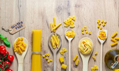 Farklı türde makarna, domates, yağ ve glütensiz etiketli tahta kaşıklar.