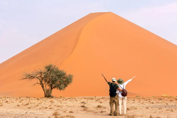 オレンジ色の砂の砂丘の近くに立っているカップル旅行者 旅行砂漠のコンセプト ストック画像