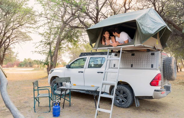 砂漠のキャンプでピックアップ4X4車の屋根に位置するテントに横たわる若いカップル ストック写真