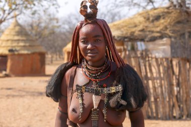 Kırsal Namibya - 22 Ağustos 2023. Genç Afrikalı bir kadın Namibya 'daki Himba kabilesinin geleneksel saç stili, deri kolyeler ve koyu renkli deri macunu giyiyor..