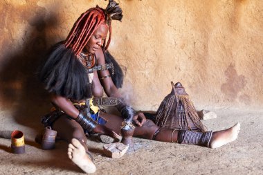 Namibya - 22 Ağustos 2023: Himba kadını, Kamanjab, Namibya, Afrika yakınlarındaki geleneksel Himba köyünde her gün kulübesinde duman banyosu yapıyor..
