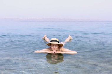 Ölü Deniz 'in tuzlu suyunda dinlenen şapkalı kadın.