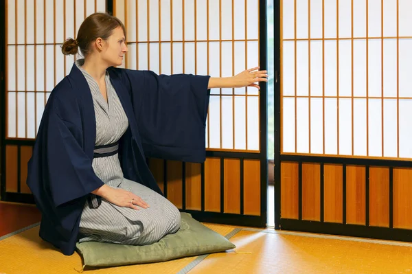 Traditional japanese house or ryokan with gaijin caucasian woman in kimono and tabi socks opening shoji sliding paper doors sitting on tatami mat floor