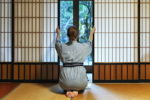 Traditional japanese house or ryokan with gaijin caucasian woman in kimono and tabi socks opening shoji sliding paper doors sitting on tatami mat floor