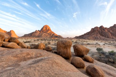 Güneş doğarken mavi gökyüzüne karşı Spitzkoppe bölgesinin ünlü yuvarlak kırmızı granit kayaları çöl manzarası. Spitzkoppe, Namibya 'da sakin bir sabahta kayalık çöl fotoğrafı