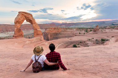 Gezintiye çıkmış bir çift. Dağın tepesinde oturan adam ve kadın güzel manzaraya bakıyor. Narin Kemer, Moab, Utah, Arches Ulusal Parkı.