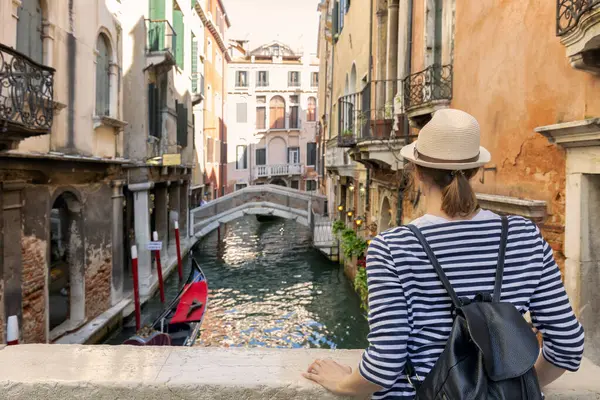 Şapkalı zarif bir kadın Venedik, İtalya 'da geçen gondollu bir kanalın tadını çıkarıyor.
