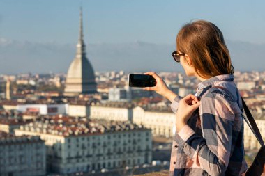 Torino 'nun (Torino, İtalya) panoramik fotoğrafını çeken turist, kentin üzerinde Köstebek Antonelliana' nın simgesi olan bir şehir merkezi. Kadın fotoğraf çekmek için akıllı telefon kullanıyor..