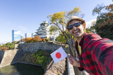 Man young travel tourist take a selfie with japan's flag at Osaka Castle, Osaka Castle is one of the most famous landmarks in Japan and Osaka, holiday lifestyle. clipart