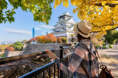 Mutlu turistler, sonbahar yapraklarıyla çevrili Osaka Kalesi 'nin önünde eğleniyor. Özgürlük ve Asya 'ya seyahat kavramı. Arka plan bulanık. Osaka Kalesi Japonya ve Osaka 'nın en ünlü simgelerinden biridir.