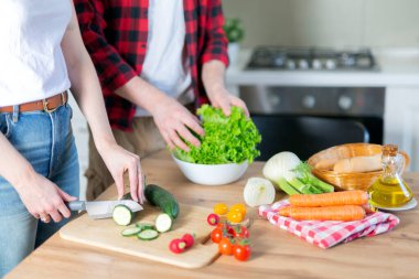 Genç bir çift mutfak masasında salata hazırlıyor, çeşitli renkli sebzeler kesiyor, vejetaryen yemekleri yiyerek sağlıklı bir yaşam tarzı sürdürmeye çalışıyor..