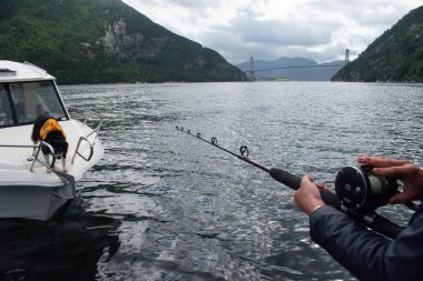 Female Fishing offshore on a boat with fishing rod and reel with mountains and fjords in background 