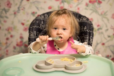 The baby eats food on his own. The child is learning to eat. Kid eating pasta