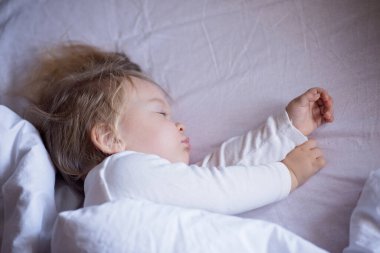 The baby is sleeping in bed. The child lies on a light blanket.