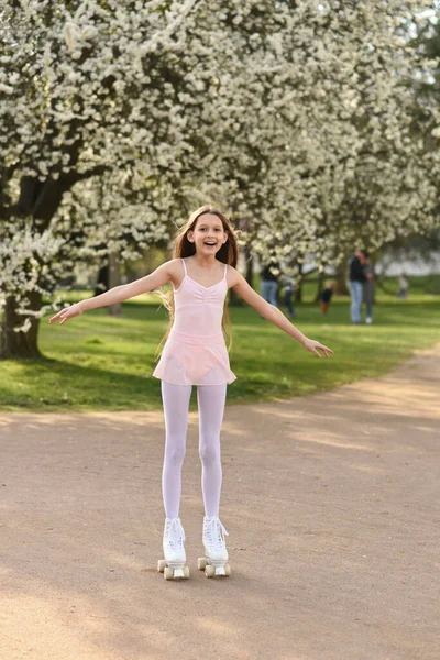 快乐的十多岁女孩在春天的公园里滑旱冰 树上开满了花 — 图库照片
