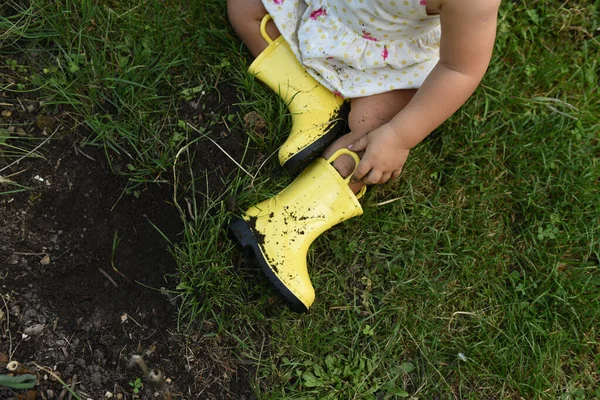 子供の足の上に黄色のゴムブーツ 草の上や黒い土の上の庭のブーツ — ストック写真