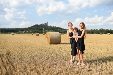 Anne ve saman yığınları olan iki kızı. Annem kızlarını kucaklıyor. Tarlada üç güzel kız