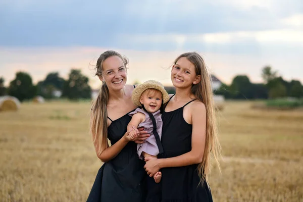 Mom with two daughters with haystacks. Mom hugs her daughters. Three beautiful girls in the fields
