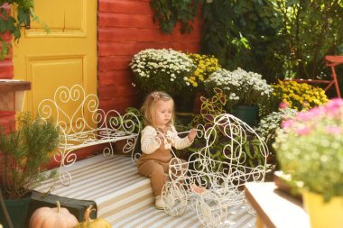 Güzel küçük bir kız bahçede bir bebek arabasıyla oynuyor. Çiçekli bahçe