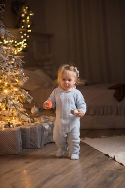 Noel ağacının arka planında Noel süsleri olan küçük bir kız. Mutlu yıllar.