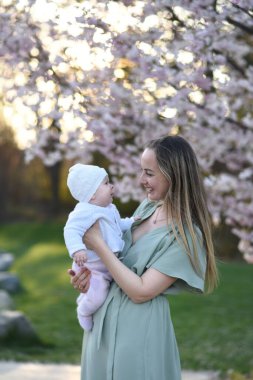 Güzel genç bir anne bebeğiyle birlikte bir bahar parkında yürüyor. Annesinin kollarında küçük bir çocuk. Yenidoğan annesiyle oynuyor.