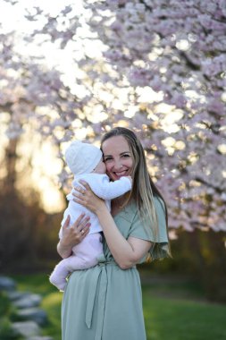 Güzel genç bir anne bebeğiyle birlikte bir bahar parkında yürüyor. Annesinin kollarında küçük bir çocuk. Yenidoğan annesiyle oynuyor.
