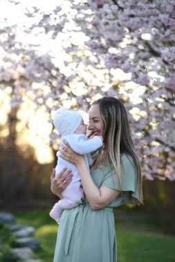 Güzel genç bir anne bebeğiyle birlikte bir bahar parkında yürüyor. Annesinin kollarında küçük bir çocuk. Yenidoğan annesiyle oynuyor.