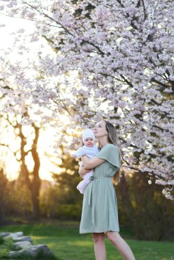 Güzel genç bir anne bebeğiyle birlikte bir bahar parkında yürüyor. Annesinin kollarında küçük bir çocuk. Yenidoğan annesiyle oynuyor.