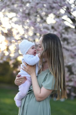 Güzel genç bir anne bebeğiyle birlikte bir bahar parkında yürüyor. Annesinin kollarında küçük bir çocuk. Yenidoğan annesiyle oynuyor.