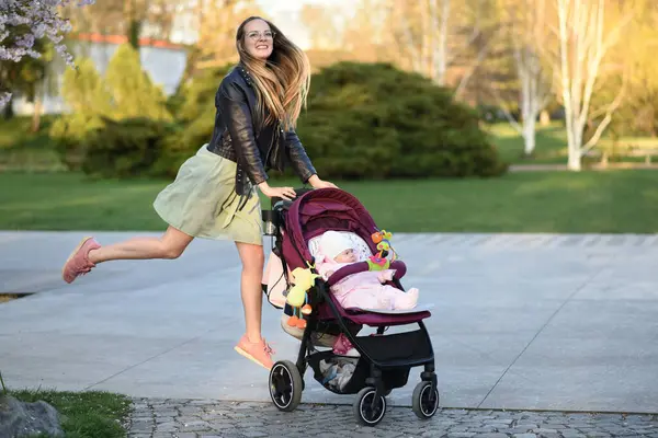 A beautiful young woman walks in the park with a baby stroller. Mom and little child on a walk