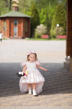 Pembe elbiseli küçük kız. Pembe çiçekli küçük kız. Parkta yürüyen küçük kız. Sarışın, iki yaşında güzel bir kız bahçede yürüyor..