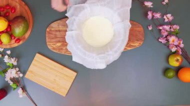 Kadın mascarpone peynirini gazlı bezle sarıyor. Mascarpone peyniri yapma süreci. Masanın üst görüntüsü. Mutfakta yemek pişirmek..