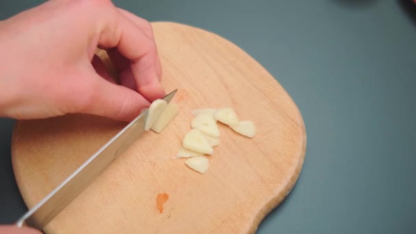 女性はナイフでニンニクを切断ボード上の小さな部分に切断します テーブルを閉じる キッチンで料理する — ストック動画