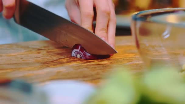 カッティングボードにナイフで赤い玉ねぎを切る女性 テーブルのクローズアップショット キッチンで料理する — ストック動画