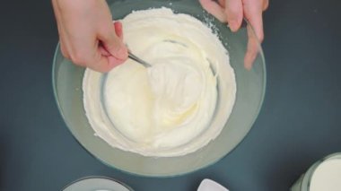 Kadın elleri bir kaşıkla karıştırılır. Pasta için yumuşak ve pürüzsüz bir krema kütlesi. Mutfak masasının üst manzarası. Mutfakta yemek pişirmek.