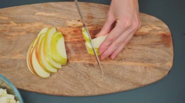 Bir kadın kesme tahtasıyla bir elmayı ince dilimlere ayırıyor. Mutfak masasının üst manzarası. Mutfakta yemek pişirmek..