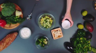 Kadın salatalık ve brokoliyi marul yapraklarının üzerine yayar. Vejetaryen salatası pişiriyorum. Mutfak masasının en üst görüntüsü. Mutfakta yemek pişirmek..