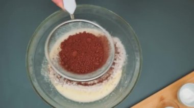Dişi eller kakaoyu hamurla derin bir tabağa karıştırıyor. Mutfak masasının üst manzarası. Mutfakta yemek pişirmek.