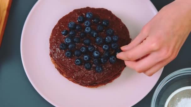 女性はブルーベリーでチョコレートケーキを飾ります ダイエット低カロリーケーキ キッチンテーブルのトップビュー キッチンで料理する — ストック動画