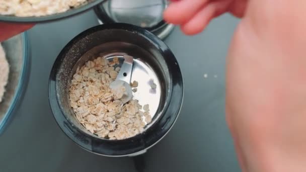 オートミールをコーヒー粉砕機にスプーンを手渡す キッチンテーブルのトップビュー キッチンで料理する — ストック動画