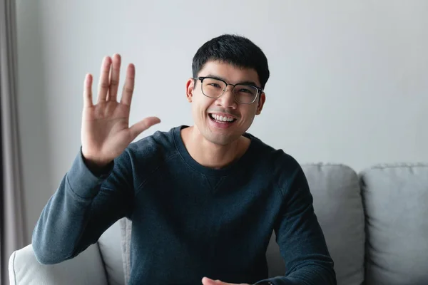 在客厅 会议室 视频会议上 年轻的亚洲男人戴着大大的眼镜 面带微笑 看着镜头 感到快乐而积极 图库图片
