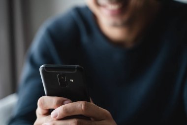 man using smartphone on sofa in living room at home, searching data and social media on internet.