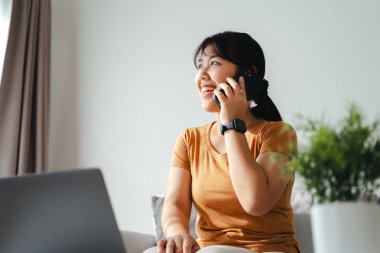 Akıllı telefonlu mutlu bir kadın ev ofisinde ya da iş yerinde dizüstü bilgisayar kullanıyor..