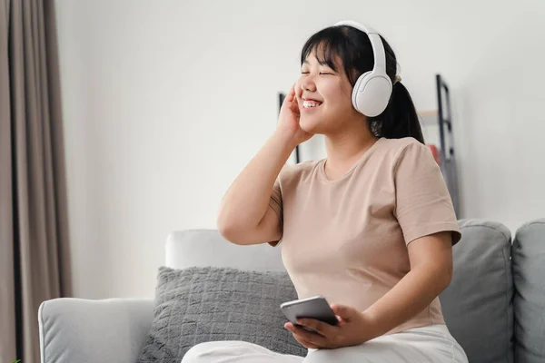 stock image Young woman listening to music with headphone and relaxing while sitting on the sofa at home.