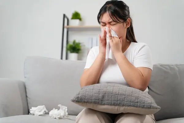Young woman got a nose allergy sneezing sitting on the sofa at home.  Flu, Influenza, Sick, Fever, Illness. Healthcare and medical concept.