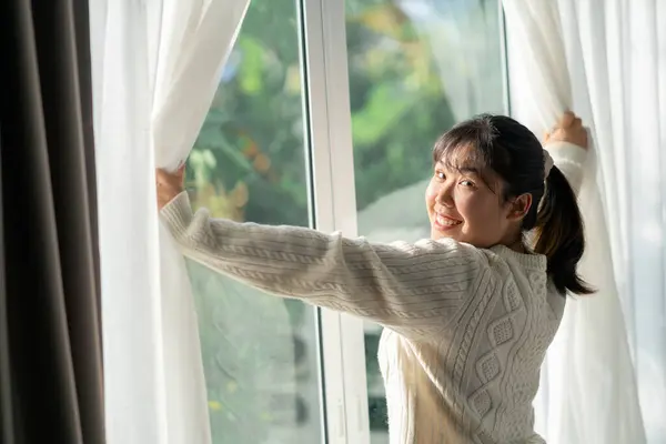 Happy woman opening window curtains in the morning at home.