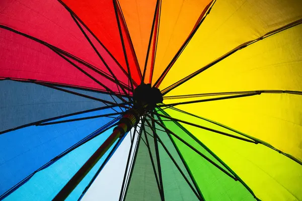A rainbow umbrella with a black handle. The umbrella is open and the colors are vibrant. Concept of joy and happiness, as the rainbow colors are often associated with positivity and good luck