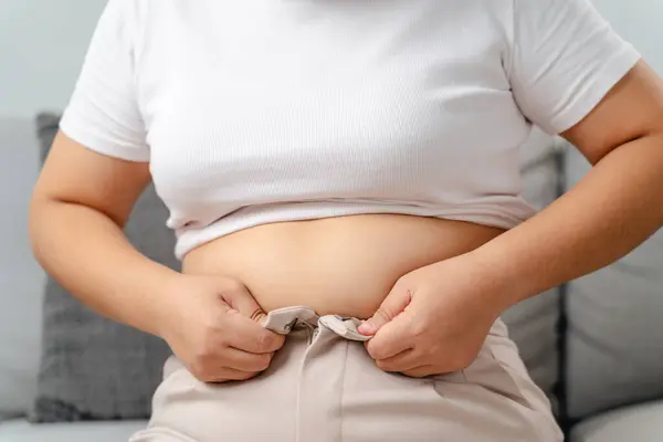 Koca göbekli şişman kadın dar pantolon, kilolu, kilo almış, sağlıklı ve tıbbi konsept giymeye çalışıyor..