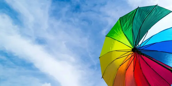 Colorful rainbow umbrella on blue sky background. LGBT, Pride Month, diversity, Sunprotect Concept.