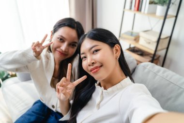İki kadın gülümsüyor ve evdeki oturma odasındaki kanepede selfie çekiyorlar. Sahne mutlu ve dostane.